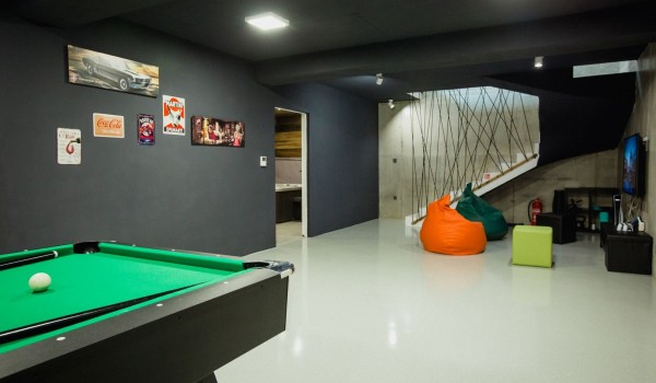 A room decorated in black tones with a pool table, green and orange beanbags and a playstation