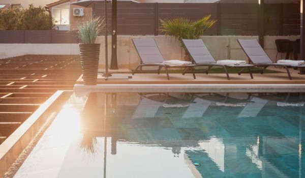 An outdoor swimming pool surrounded by deck chairs and a parasol on the outdoor terrace of a modern villa with a view of the mountains on the island of Krk