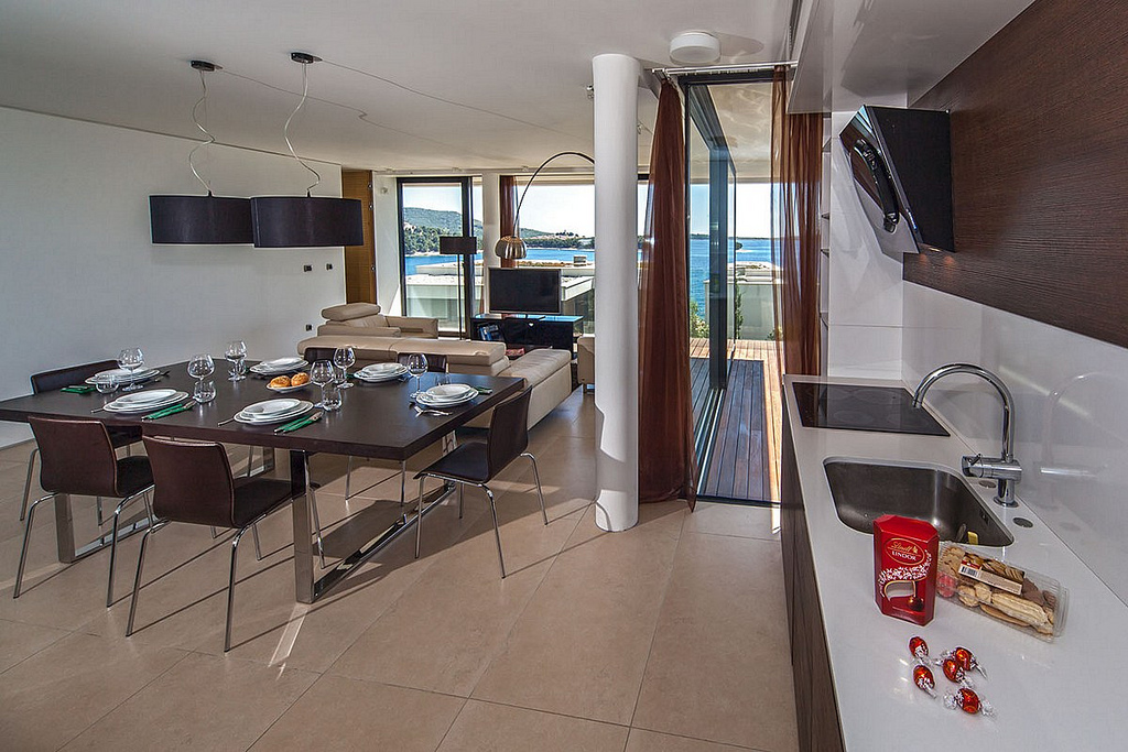The interior of the luxury apartment Biseri Jadrana 3 with a kitchen, a dining table with chairs and a living room with a view of the sea in Primosten