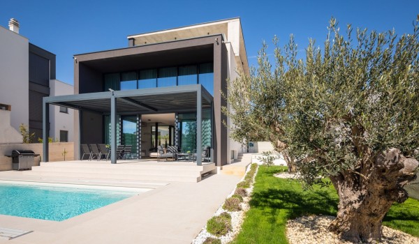 Front view on the property of Luxury Villa Sea and View Idria with an olive tree in the first plan, swimming pool, a terrace with dining set, seating area and a barbecue