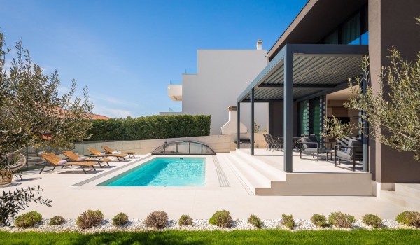 Side view on greenery, a pool with patio and loungers and a terrace equipped with a dining set, a seating area and electronic pergola system
