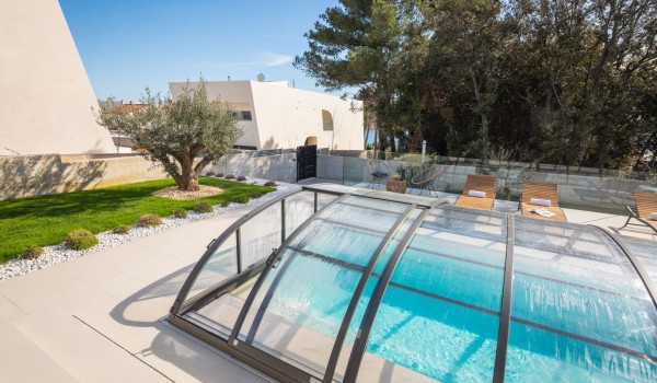 A view from the terrace with pergola on a covered private hydromassage heated pool, modern pavement and a dense pine tree forest patch in front of the property