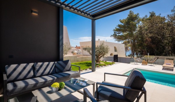 Main Terrace of the Villa Idria with a piece of comfy outdoor furniture and a coffee table overlooking the pool area with loungers and pine forest next to the property