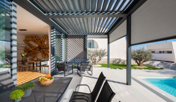 A view of the interior and the terrace of the Villa Idria with a leisure and dining area with a modern electronic pergola system for a fine adjustment of shade