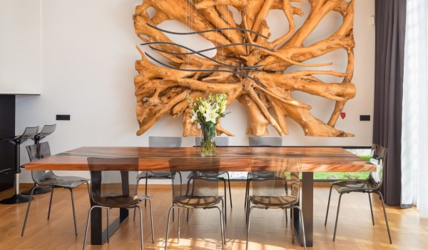 A massive root of acacia tree on the wall of the dining  area with a table and 8 modern translucent  grey chairs on the ground floor of the Villa Idria Sea and View