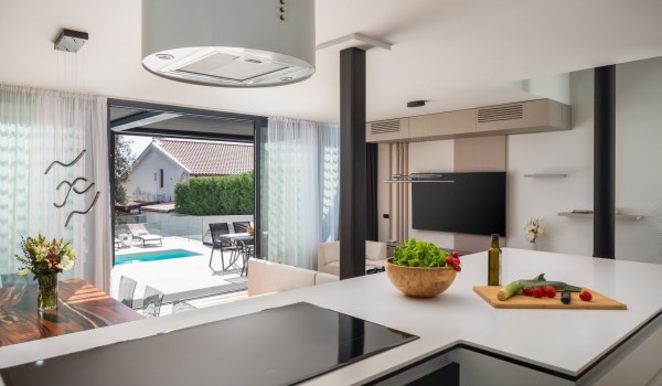 Modern cylindrical hood above the ceramic stove of the kitchen island with a view on the living room and exterior of the Luxury Villa Idria Sea and View Petrcane
