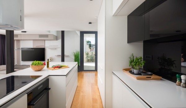 A view from the fully equipped kitchen with modern high tech appliances, a living room with a SMART LCD TV and doors to a side terrace with breakfast table with chairs