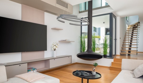 Living room with comfortable sofas, SMART LCD TV and a minimalistic modern fireplace next to the glass panels and exit to the side terrace and floating stairs