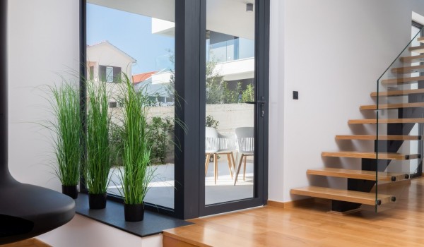 A view from the living area showing beautiful floating staircase and a large framed floor-to-ceiling window next to the exit on a side terrace with table and chairs