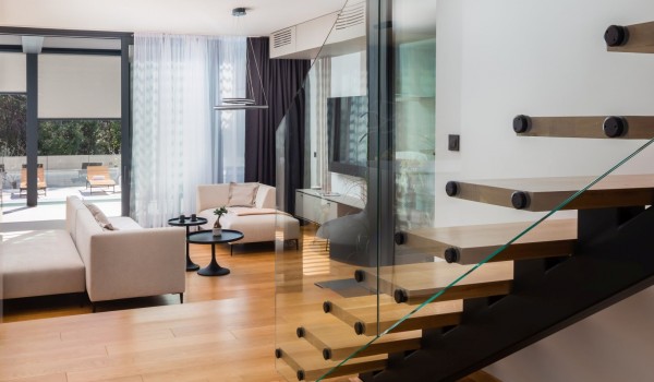 Seating area with comfortable sofas in the living room with SMART TV and a gaming console, a view through the clear glass panels which run the length of the staircase enhancing the open conce