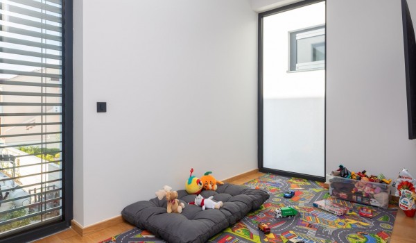 Children's play area on the first floor equipped with toys, a colorful carpet and an LCD TV, two floor-to-ceiling glass panels with shades