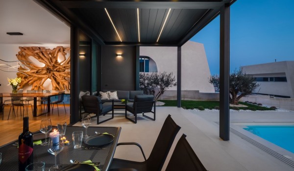 Side view on bot interior and exterior of the Villa Idria SEa and View - a dining room with a large wooden decoration on the wall and a roofed terrace with dining set and comfortable seating