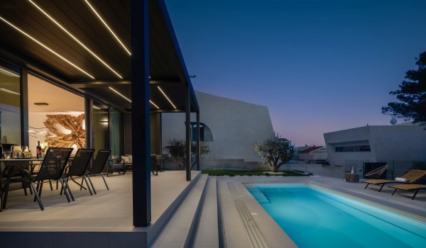 A terrace with dining area and electronic pergola with a view indoors on a dining room wall with a large decoration, pool on the right part of the photo