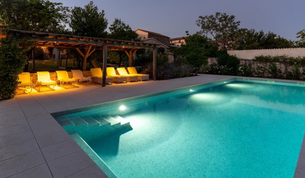 Illuminated private pool surrounded by sun loungers in the roofed part of the terrace of the luxury vacation villa Deluxe Manor Baderna