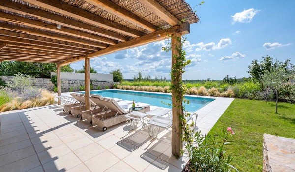Greenery in the private fenced garden with pool surrounded by sun loungers and a roofed part of the paved terrace