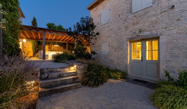 External stone steps leading to a terrace with a dining table and outdoor seating in front of the entrance to the main house of the Deluxe Manor Baderna holiday villa in Radovani