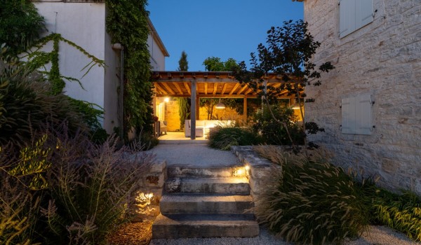 Gravel path to the illuminated roofed terrace in front of the family vacation and rental villa Deluxe Manor Baderna