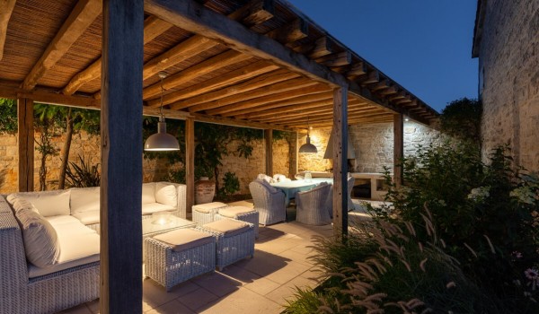 Fenced roofed terrace with seating, outdoor table and chairs and outdoor grill in front of the entrance to the stone family villa in Istria