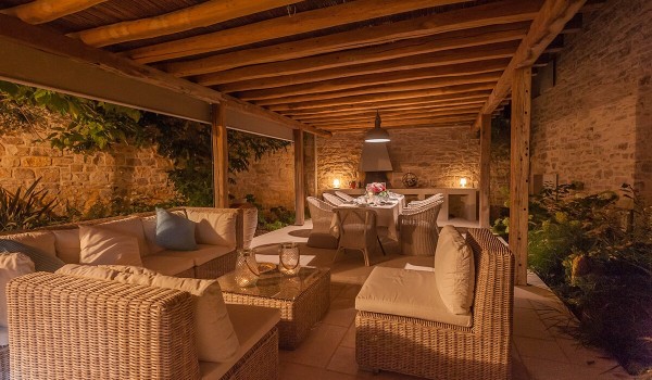 Roofed part of the patio with seating area, table and chairs and an outdoor grill in front of the luxury holiday villa Deluxe Manor Baderna