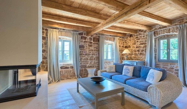 Comfortable sofa with a coffee table in front of a modern indoor fireplace in the charmingly decorated living room of a family villa with pool in Radovani