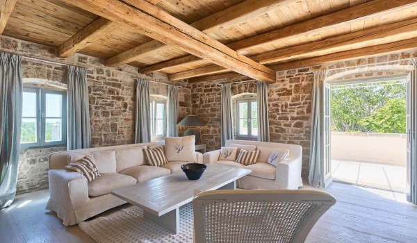 Rustically decorated living room with a white couch and two-seater, a stone wall and a wooden ceiling in the Deluxe Manor Baderna holiday villa in Istria