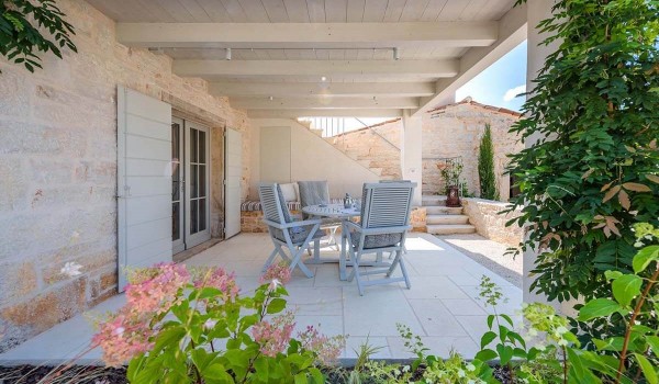 Outdoor wooden table with chairs on the roofed part of the terrace in front of the entrance to the guest house on the property of the villa Deluxe Manor Baderna in Radovani