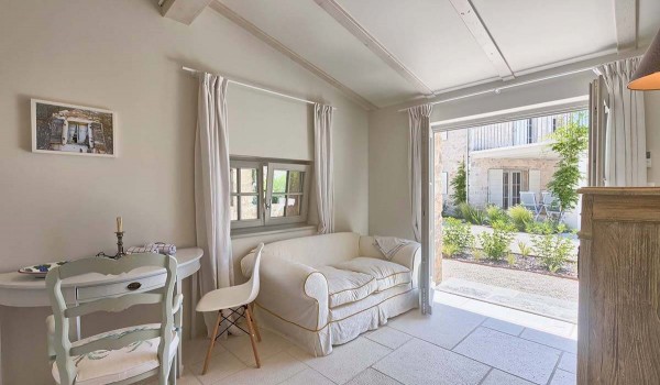 Living area with a white two-seater and a dining table and an exit to the landscaped yard of a luxury stone holiday villa in Radovani