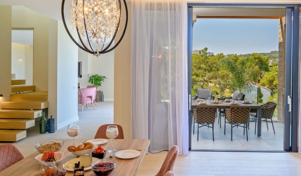 The interior of a modern kitchen with a dining area and a view of the private lounge terrace of the family holiday villa for rent by the sea Raquel