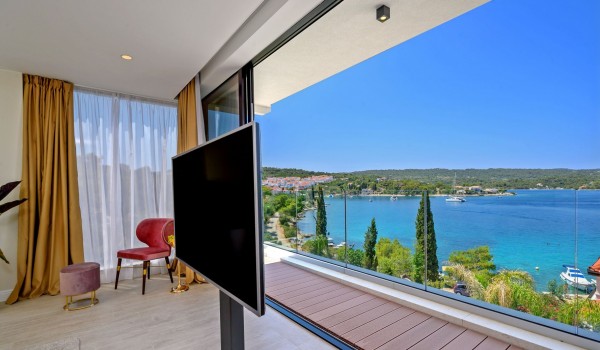 A spacious bedroom with a king size bed, a lounge chair and a SMART TV of a family  holiday villa on Šolta by the sea