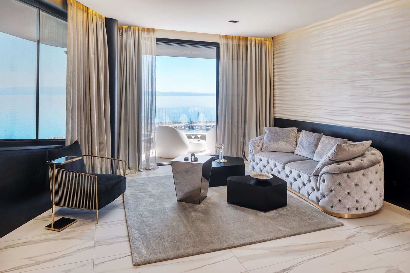 Glamurozno uređen dnevni boravak sa sivom komfornom sofom foteljom stolićem i pogledom na lučicu u luksuznom apartmanu za najam u Splitu