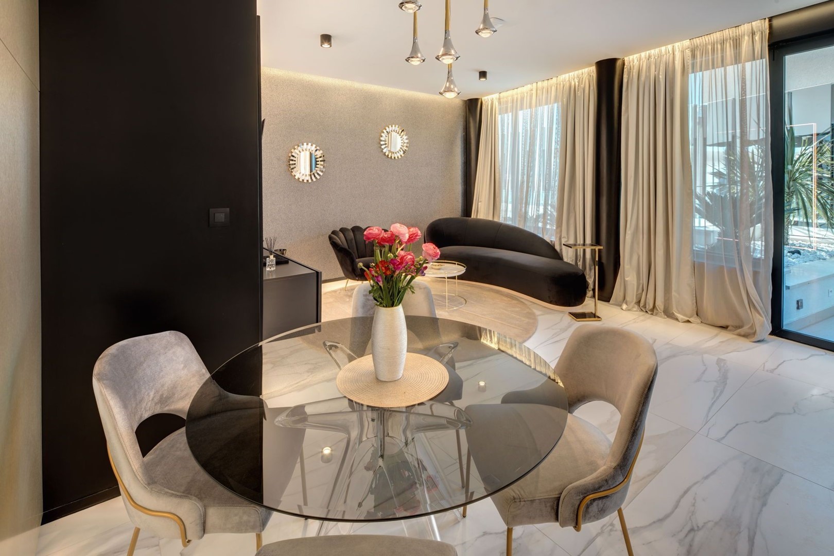 Interijer luksuznog apartmana Split Gem Gold sa staklenim stolom i stolicama te prostorom za sjedenje sa crnom sjedećom garniturom i sofom u obliku školjke