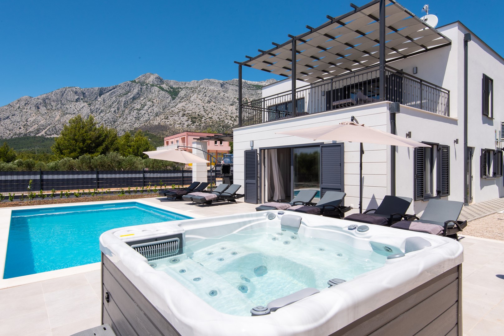 Pogled na jacuzzi te na privatni bazen okružen ležaljkama za sunčanje na vanjskoj terasi luksuzne vile za najam i odmor Callisto Orebić