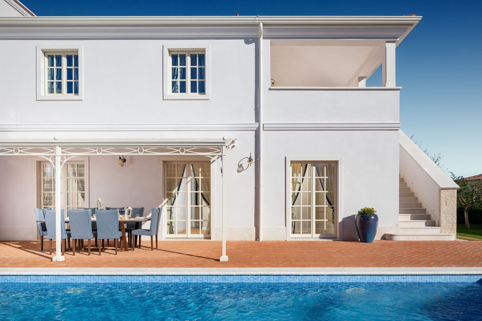 Pogled na privatni bazen i vanjsku terasu sa blagovaonskim stolom i stolicama u luksuznoj vili Azzurra u Istri