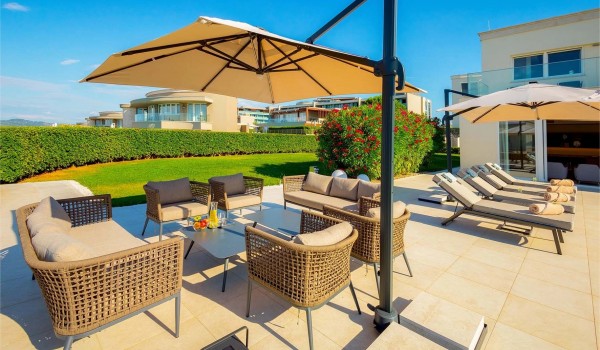 Outdoor seating area with table and parasol next to sun loungers around a large heated pool in front of the entrance to the ground floor of the newly built villa Residenzia Imperiale near Uma