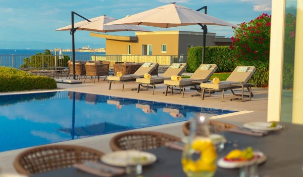 View from the outdoor dining table to the private paved terrace with a large heated pool surrounded by sun loungers and parasols in front of the newly built holiday villa Residenzia Imperiale