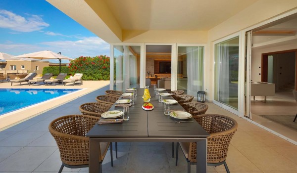 Large outdoor dining table with chairs in the roofed part of the private paved terrace of the luxury villa Residenzia Imperiale in Savudrija