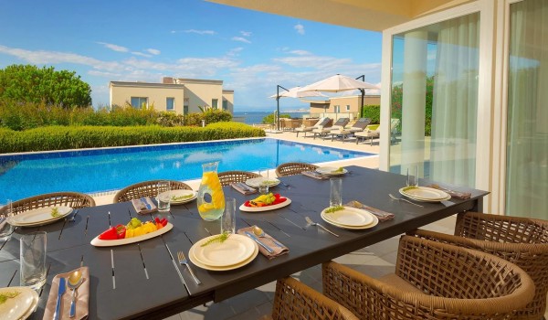 View from the outdoor dining table to the heated pool surrounded by sun loungers on the fenced terrace of the luxury villa Residenzia Imperiale in Istria