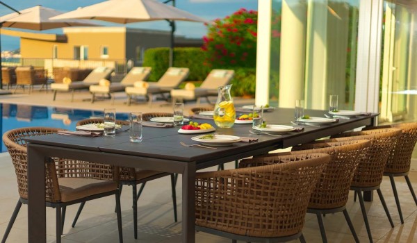 Roofed part of the outdoor terrace with a dining table and chairs next to the private heated pool surrounded by sun loungers