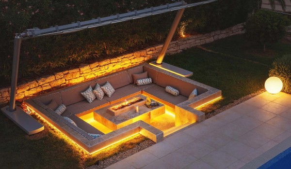Illuminated outdoor fire pit with seating area and retractable canopy in fenced yard next to private heated pool