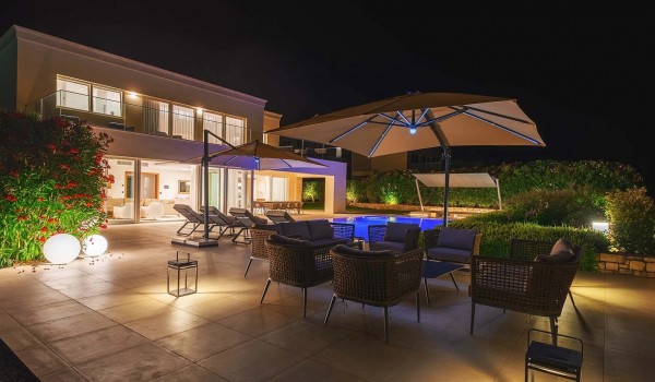 Outdoor seating area with parasol on the illuminated private terrace with heated pool and sun loungers in front of the luxury villa Residenzia Imperiale