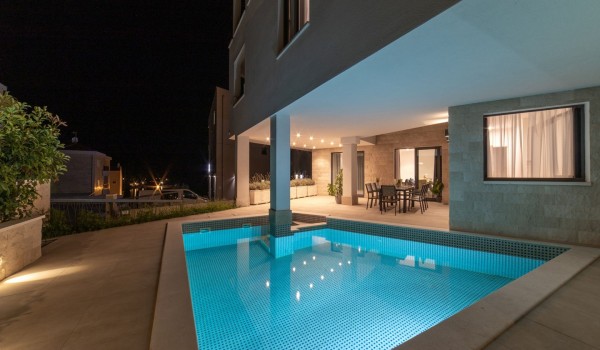 Night view of a private pool and dining table on the terrace in a Croatia luxury sea view villa with gym and sauna in Trogir