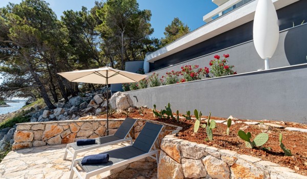 Two sun loungers on a secluded sunbathing area surrounded by stone-walls and parasols in front of the beachfront luxury villa Miracul Korcula