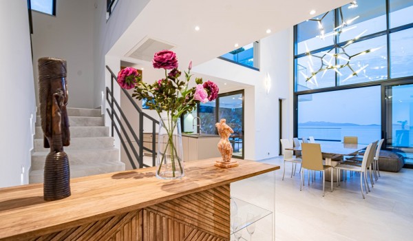 The elegant open-space airy ground floor of a luxury holiday rental villa with a sea view, a dining area, and a large glass walls