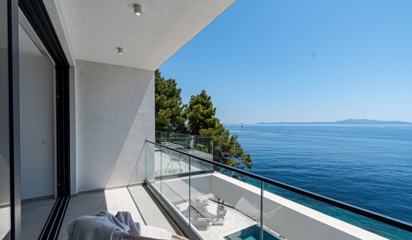 A view on the comfy seating on a balcony and a pool patio by the infinity pool in front of the luxury seafront villa for family vacations on Korcula