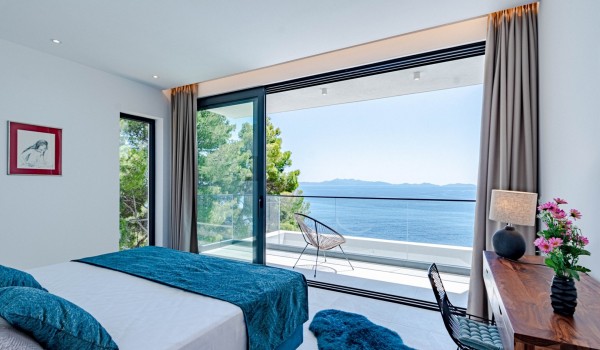 Modern luxurious decorated airy bedroom with a king-size bed and access to the spacious balcony with an outdoor armchair