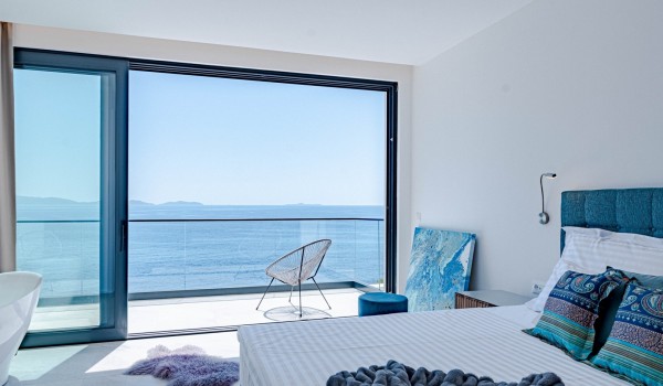 Modern luxurious decorated airy bedroom with a king-size bed, a desk with a chair and access to the spacious balcony overlooking the sea