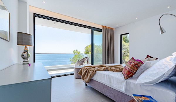 Elegant airy bedroom with a king-size bed, a desk with a chair and access to the spacious balcony overlooking the sea