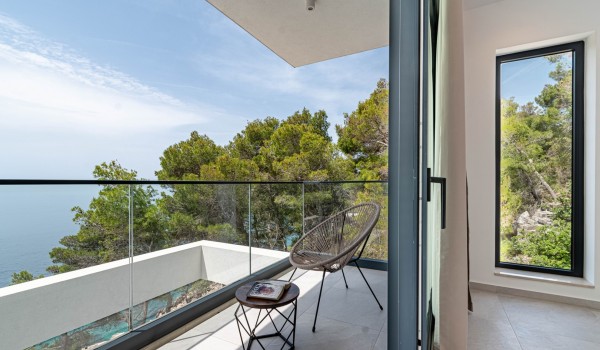 Exit from the bedroom through the glass wall onto a balcony with a chair and a small table overlooking the sea in Korcula luxury villa with total privacy