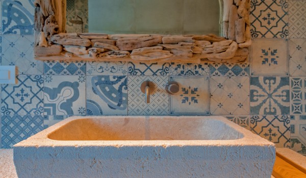 A view of a marble sink with picturesque tiles and a mirror with a wooden frame in the bathroom of the luxury villa Bliss