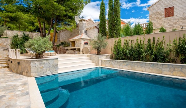 A view of the spacious pool next to which there is a fireplace and two deckchairs on the property of the luxury villa Brač